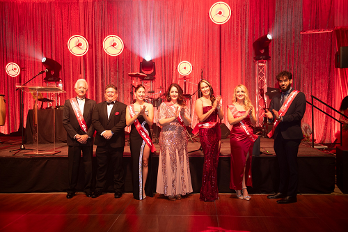 Group of people standing in front of stage each wearing a Leader of Impact sash.